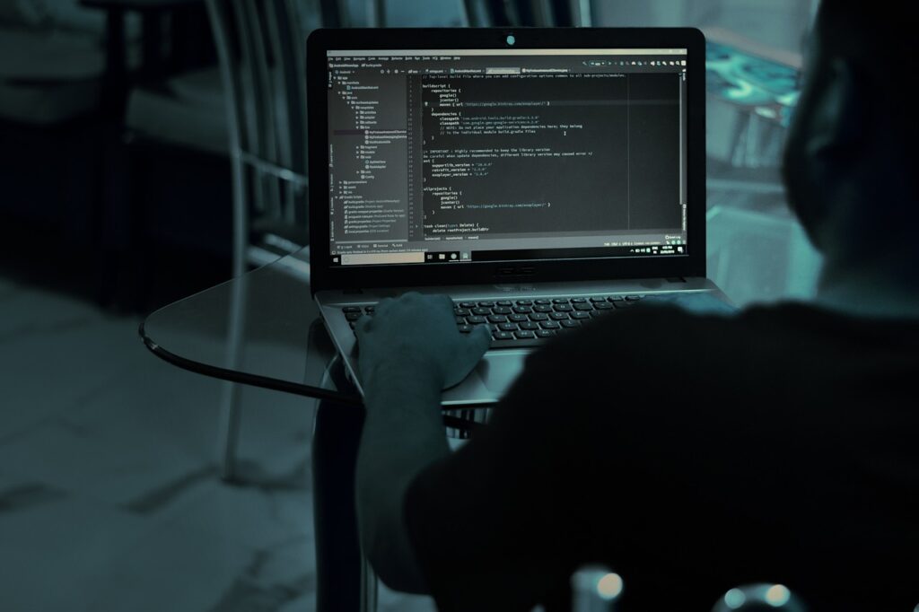 Een man die aan een tafel zit te programmeren op zijn laptop.